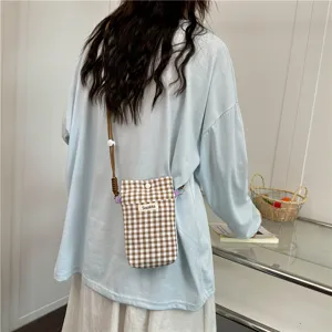 Detailed shot of a brown and white checkered crossbody phone bag worn by a model in lifestyle.