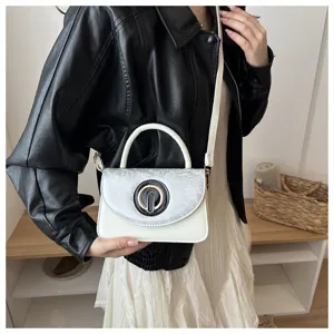 Primer plano detallado del elegante bolso cruzado blanco con cierre metálico circular.
