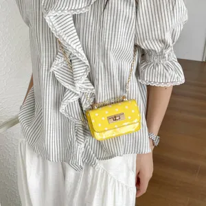 Yellow polka dot patent leather crossbody mini bag detail view with gold chain and twist lock.