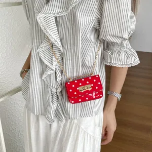Close-up detail of the stylish red polka dot crossbody bag with gold chain strap and metal lock.