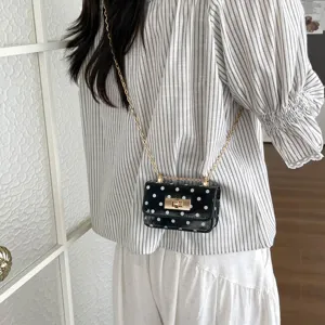 Detailed shot of a chic black polka dot mini crossbody bag with gold chain and turn-lock.