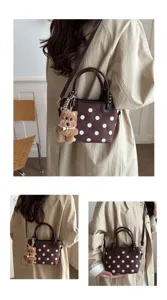 Détail de sac seau à pois marron montrant un style d'épaule croisé et un joli pendentif d'ours.