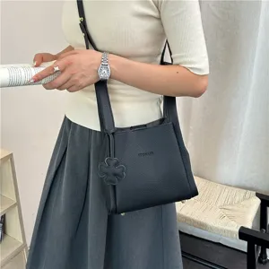 Close-up detail shot of black leather bucket bag with cute clover charm worn by model.