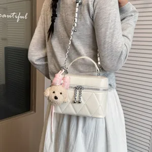 Detailed shot of a white quilted vanity crossbody bag with a chain strap and cute plush charm.