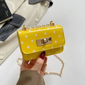 Close-up shot showing the vibrant yellow polka dot handbag details, metallic lock, and chain strap.
