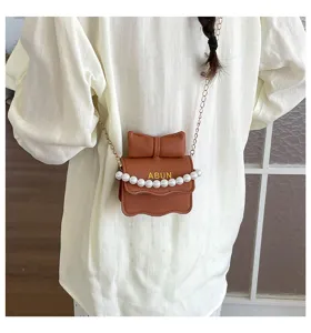 Detailansicht der braunen Umhängetasche für Kinder mit Schleife, Perlenkette und Kette.