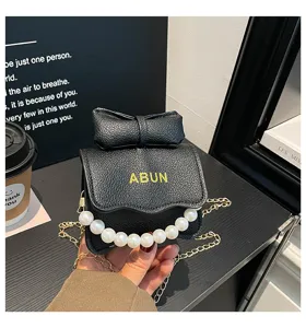 Sac bandoulière noir pour fille avec nœud mignon, poignée perle et chaîne dorée. Jolie pochette.