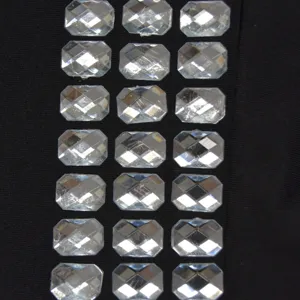 Close-up detail of sparkling rectangular rhinestone embellishment on black fabric texture.