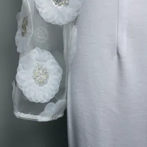 Detail van witte jurk met transparante mesh lange mouwen met 3D bloemen en glinsterende pailletten.