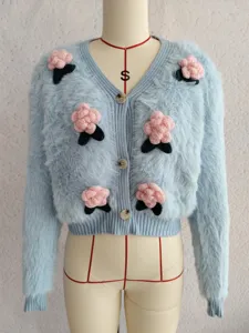 Hellblaue flauschige Strickjacke Detail mit süßen 3D rosa Blumen Häkelarbeit und Knöpfen.