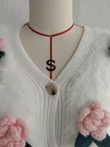 Detailansicht der weißen Strickjacke mit 3D rosa Häkelblumen und einem Knopf.