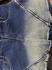 Denim skirt detail featuring gradient wash, diagonal zippers, frayed hem and contrast stitching.