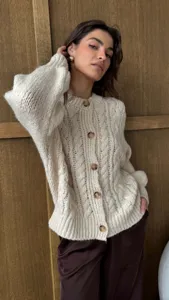 Detailopname van een gezellig crème chunky kabelgebreid vest met klassieke knopen.