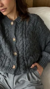 Gedetailleerde close-up van een donkergrijze kabelbreisel cardigan met knopen en textuur.