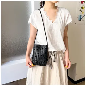 Vue détaillée d'un élégant sac bandoulière noir tressé porté par un mannequin stylé.