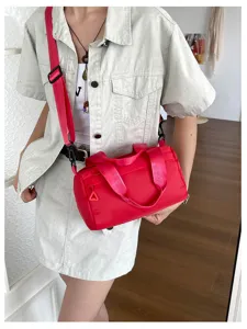 Detalle de bolso bandolera cilíndrico rojo, correa elegante y diseño con cremallera.