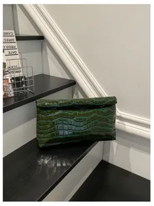 Dark green crocodile pattern clutch bag detail, minimalist chic design for women commuting.