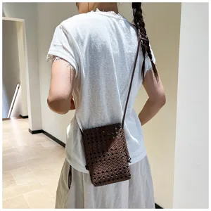 Vue détaillée d'un mini sac bandoulière en cuir tressé marron foncé porté par un modèle.