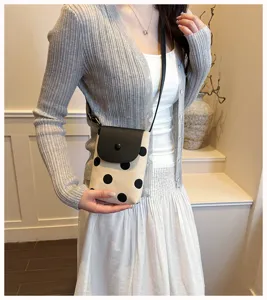 Detail view of the stylish polka dot canvas crossbody bag with black flap and thin strap.