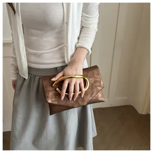 Detailansicht der bronzenen Clutch mit auffälligem goldenen ovalen Metallringgriff.