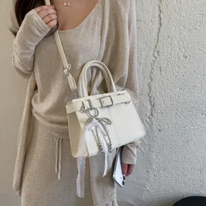 Dettaglio della borsa a mano bianca con fibbia elegante e ciondolo con perle e fiocco.