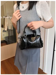 Vista detallada de un bolso Boston de charol negro con asas y correa para mujeres elegantes.