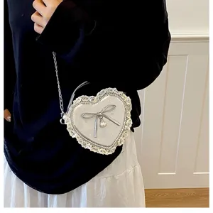 Detailed view of silver heart-shaped cross-body bag with lace trim and bow pendant.