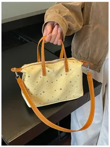 Detailaufnahme einer gelben Handtasche mit Sternenprint und braunen Ledergriffen und Gurt.