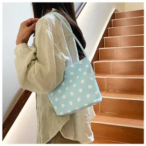 Detailed view of light blue shoulder bag with white polka dots worn in indoor scene.