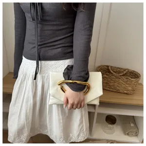 Detailaufnahme der eleganten weißen Clutch mit auffälligem goldenen Metallgriff und Leder.