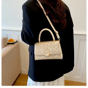 Nahaufnahme einer stilvollen beige Umhängetasche mit Monogramm-Muster und goldenem Schloss.