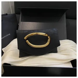 Detailaufnahme einer schwarzen Clutch mit goldenem abstraktem Metallgriff und Geschenkbox.