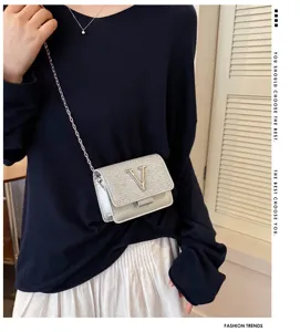 Détail d'un petit sac bandoulière argenté chic avec chaîne et logo V remarquable.