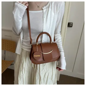 Detail van retro bruine lederen crossbodytas met metalen handvat en maanvormig accent.