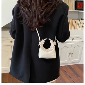 Detail view of a chic white mini crescent crossbody bag with ruffle trim and metal ring handle.
