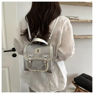 Detailed view of silver metallic mini backpack with cute lace trim and bear patch on back.