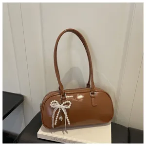 Détail du sac épaule oreille en cuir verni marron avec pendentif nœud perle et dentelle.