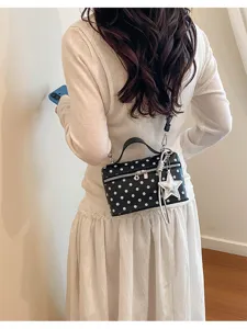 Detail shot of a stylish black and white polka dot vanity crossbody bag worn on model.