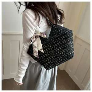 Detailopname van stijlvolle zwarte tweed tote tas gedragen op schouder met zijden sjaal.
