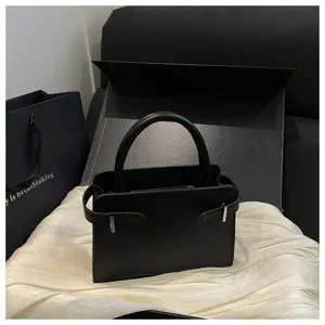 Close-up detail view of minimalist black handbag featuring side straps and metallic buckle.
