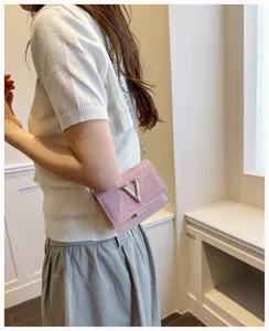 Détail du sac à bandoulière en strass rose avec chaîne argentée et logo V en métal.