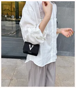 Vue détaillée du mini sac bandoulière noir avec une boucle V argentée et une chaîne.