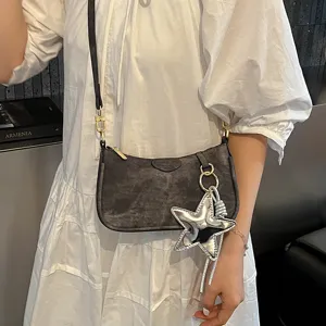Detail shot of a chic grey suede shoulder bag with a silver star pendant and gold hardware.