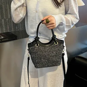 Close up view of stylish tweed bucket bag with black leather handle and chic metal rings.