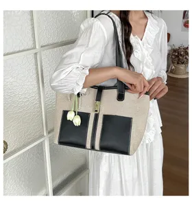 Detalle de bolso tote de lona y piel, con bolsillos frontales, cerradura y lindo colgante.