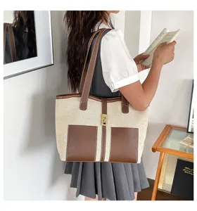 Detalle del bolso tote de lona con ribetes de cuero marrón y cierre metálico.