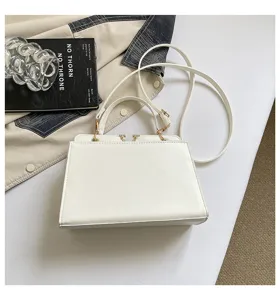 Close-up of a stylish white crossbody handbag with structured design and sleek metal hardware clasp.