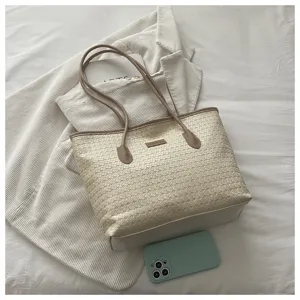 Detaillierte Nahaufnahme einer schicken beigen geflochtenen Tasche mit weißer Jacke.
