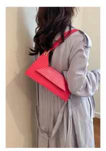 Geometric pink asymmetric crossbody bag with croc-embossed flap and metal ring accent.