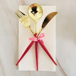 Gold-plated plastic cutlery set with pink handle and ribbon, flat lay style table tableware.